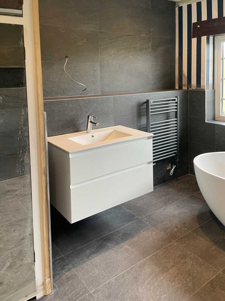 Contemporary, modern and dark coloured bathroom redesign underway in Giggleswick, Settle - showing installation of large mozzano two drawer basin unit for additional storage and new electrical work.