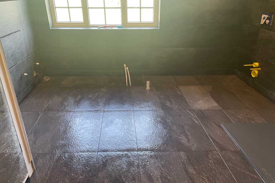 Contemporary, modern and dark coloured bathroom redesign underway in Giggleswick, Settle - showing installation of floor tiles and new pipework.